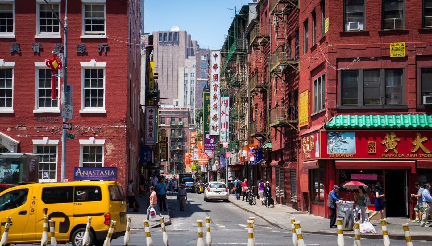 Scène de rue animée en journée à Chinatown, à New York, avec des piétons, des magasins et des taxis.