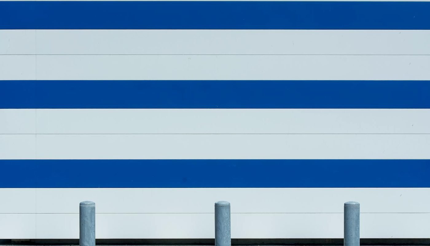 Mur minimaliste moderne avec des rayures bleues et blanches et des bornes dans un cadre urbain.