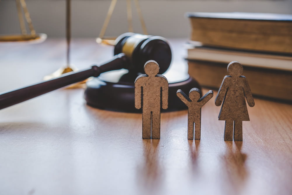 Figurines en bois représentant une famille devant un marteau de juge pour illustrer le Droit de la famille