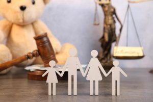 Famille en papier tenant la main devant une balance de la justice et un ours en peluche, évoquant le Droit de la famille